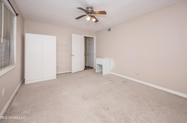 unfurnished bedroom with a textured ceiling, light carpet, visible vents, and baseboards