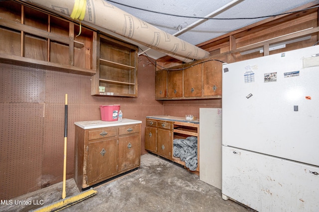 kitchen with brown cabinetry, freestanding refrigerator, light countertops, concrete floors, and open shelves