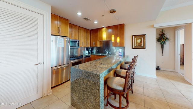 kitchen with a breakfast bar area, stainless steel appliances, dark stone countertops, decorative light fixtures, and light tile patterned floors