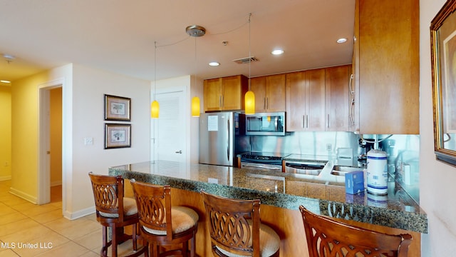 kitchen featuring kitchen peninsula, hanging light fixtures, light tile patterned floors, appliances with stainless steel finishes, and dark stone countertops