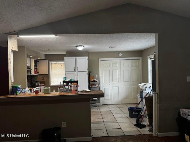 53 Flagstaff St, Lumberton, MS 39455 - kitchen with vaulted ceiling, a textured ceiling, white cabinetry, a peninsula, and light tile patterned floors