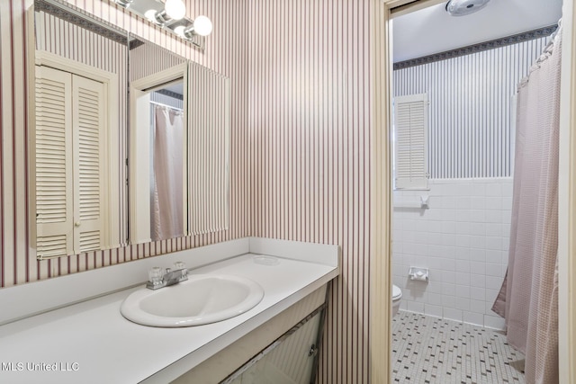 full bath with toilet, tile walls, vanity, tile patterned floors, and wallpapered walls