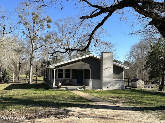 view of front of property featuring a chimney, a storage unit, covered porch, an outdoor structure, and a front lawn