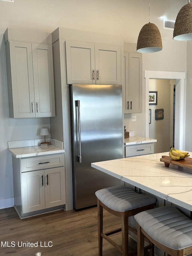 kitchen with light stone counters, high quality fridge, visible vents, a kitchen breakfast bar, and dark wood finished floors