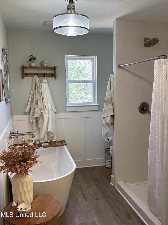 bathroom with wood finished floors, wainscoting, a shower stall, and a decorative wall