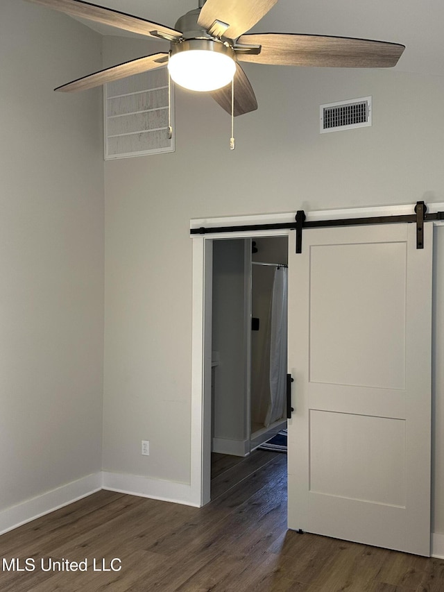 spare room featuring a barn door, baseboards, visible vents, ceiling fan, and dark wood-type flooring