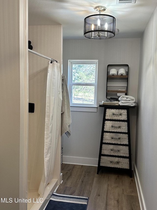 full bath with a notable chandelier, a shower stall, baseboards, and wood finished floors