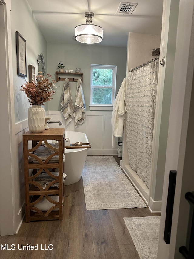 bathroom featuring a decorative wall, a wainscoted wall, wood finished floors, visible vents, and a shower stall