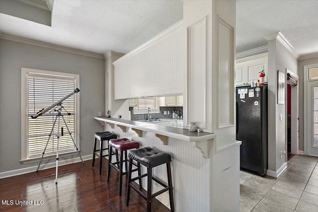 kitchen featuring a breakfast bar area, kitchen peninsula, white cabinets, and black fridge