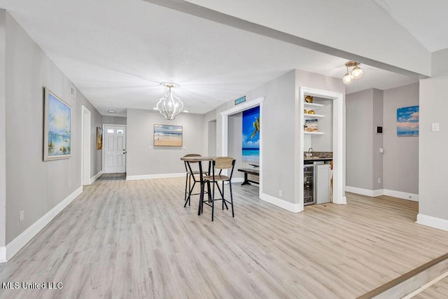 dining room with a dry bar, beverage cooler, baseboards, and light wood-style flooring