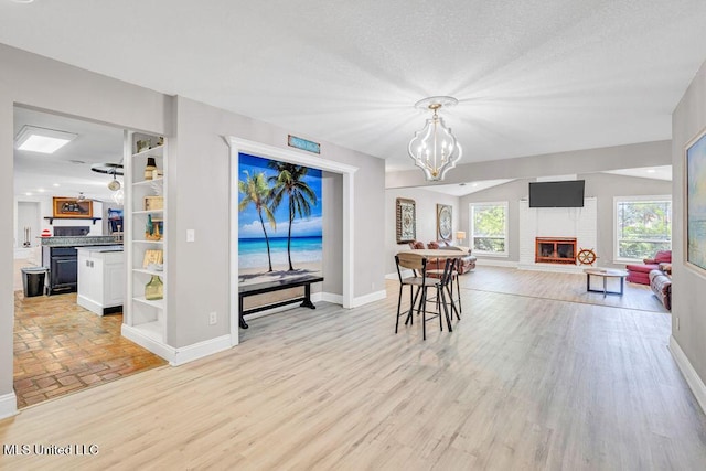 dining room with baseboards, light wood-style floors, a brick fireplace, and an inviting chandelier