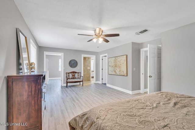 bedroom featuring light wood-type flooring, visible vents, a textured ceiling, ensuite bath, and baseboards