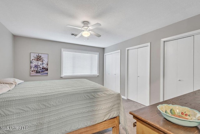 bedroom with visible vents, ceiling fan, carpet, multiple closets, and a textured ceiling