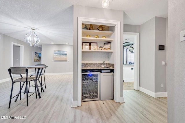 bar with wine cooler, a textured ceiling, wet bar, and light wood finished floors