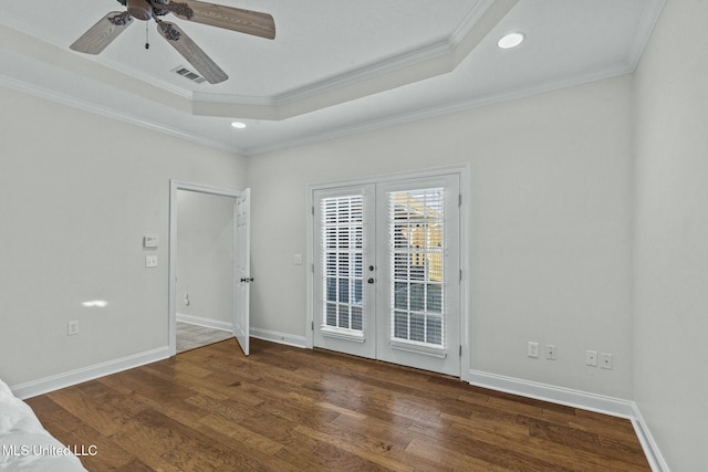 empty room featuring ornamental molding, a tray ceiling, dark wood-type flooring, and french doors