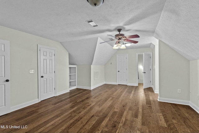 additional living space with lofted ceiling, built in shelves, dark wood-type flooring, and a textured ceiling