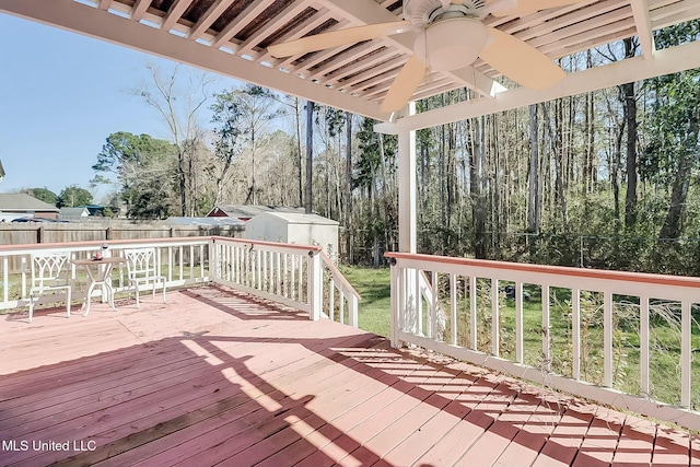 wooden terrace featuring a storage shed, ceiling fan, fence, and an outbuilding