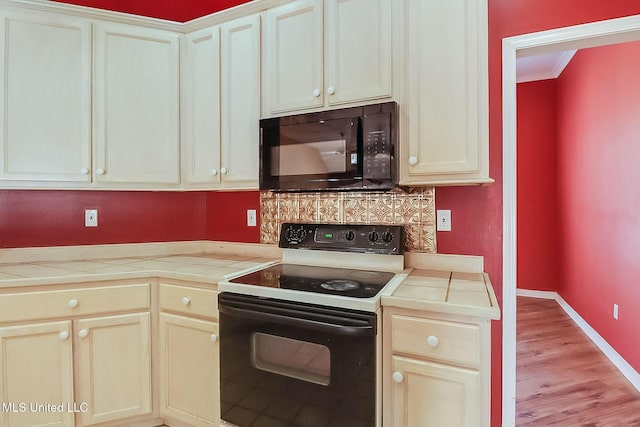 kitchen featuring tile counters, decorative backsplash, range with electric cooktop, black microwave, and baseboards