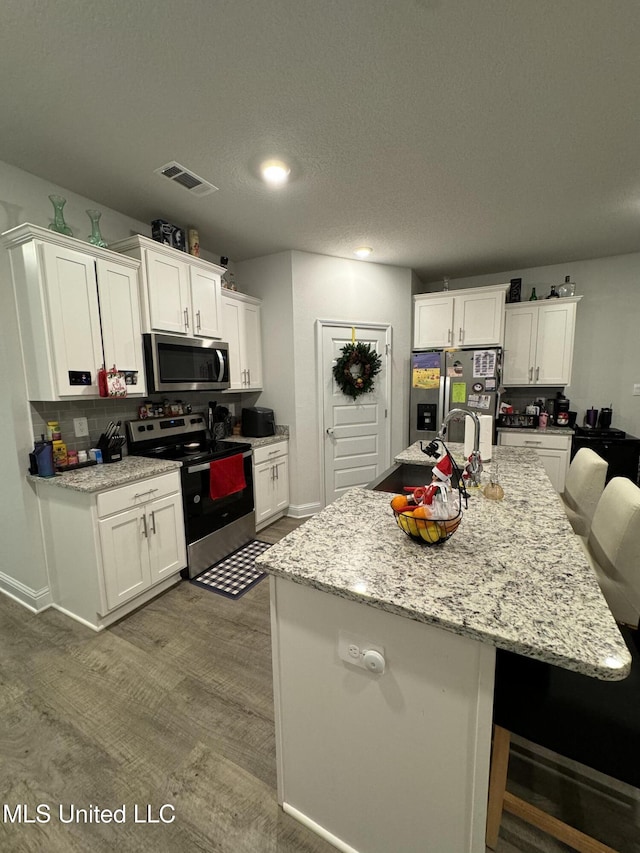 kitchen with light stone counters, white cabinetry, an island with sink, and appliances with stainless steel finishes