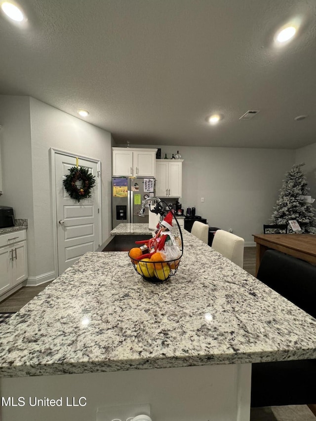 kitchen featuring a spacious island, stainless steel fridge, light stone countertops, dark hardwood / wood-style flooring, and white cabinetry