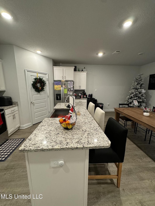 kitchen featuring a breakfast bar area, white cabinets, stainless steel fridge with ice dispenser, and an island with sink