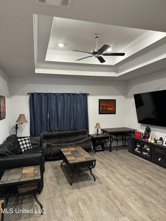 living room with ceiling fan, light wood-type flooring, ornamental molding, and a tray ceiling