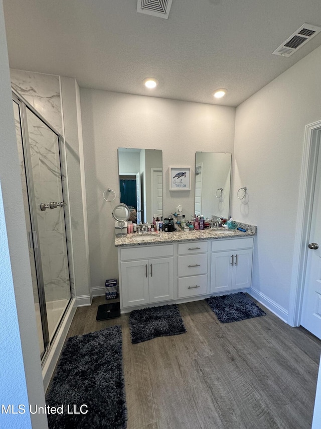 bathroom with a textured ceiling, vanity, wood-type flooring, and walk in shower