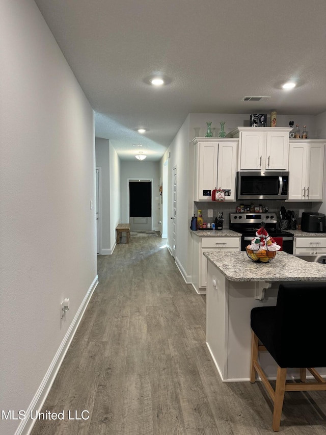 kitchen featuring decorative backsplash, appliances with stainless steel finishes, light hardwood / wood-style floors, white cabinetry, and a breakfast bar area