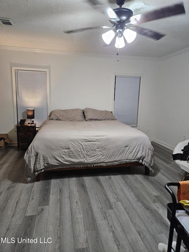 bedroom featuring a ceiling fan, crown molding, wood finished floors, a textured ceiling, and visible vents