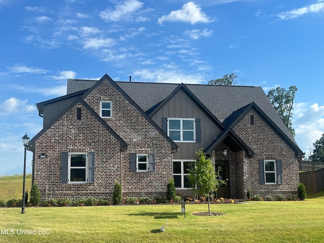 view of front of home with a front lawn, board and batten siding, a shingled roof, and brick siding