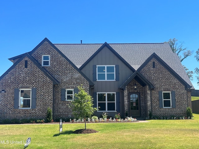 view of front of house featuring a shingled roof, a front yard, and brick siding