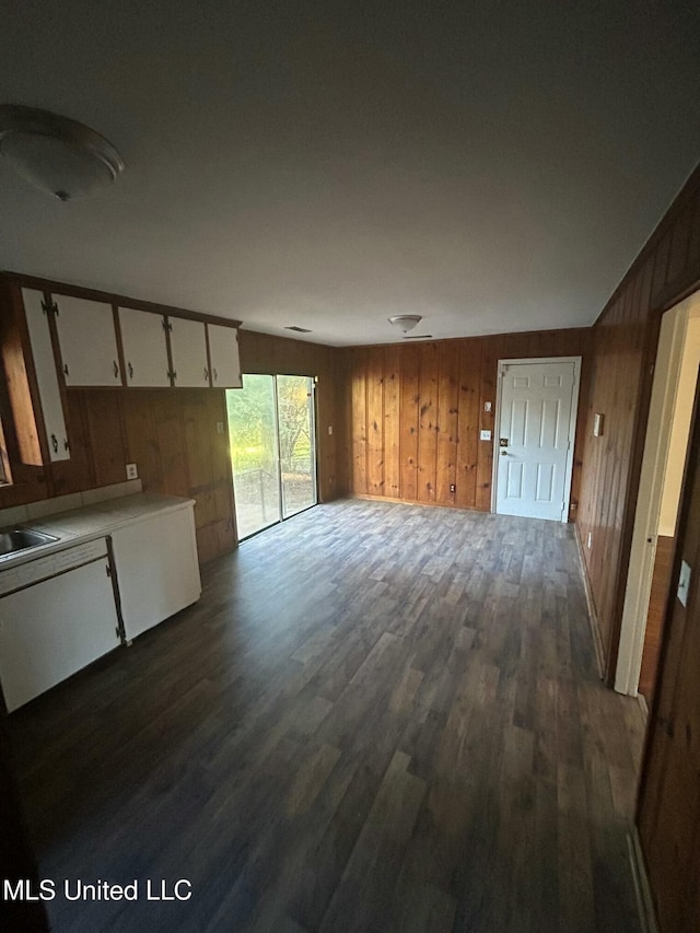 unfurnished living room featuring wood walls, dark wood-type flooring, and a sink