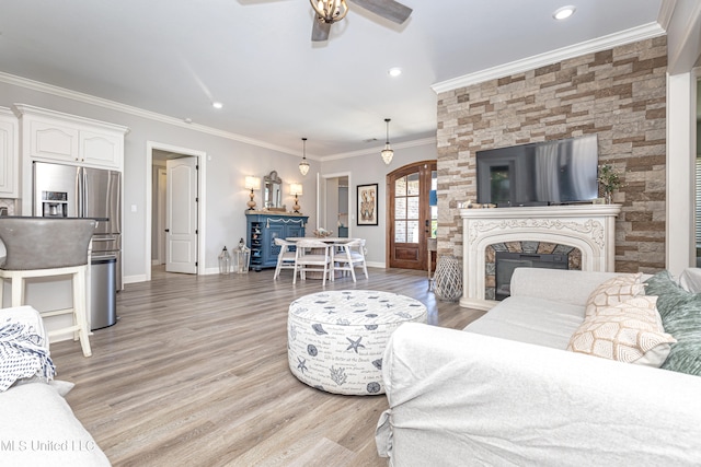 living room featuring light hardwood / wood-style flooring, ceiling fan, a fireplace, and crown molding