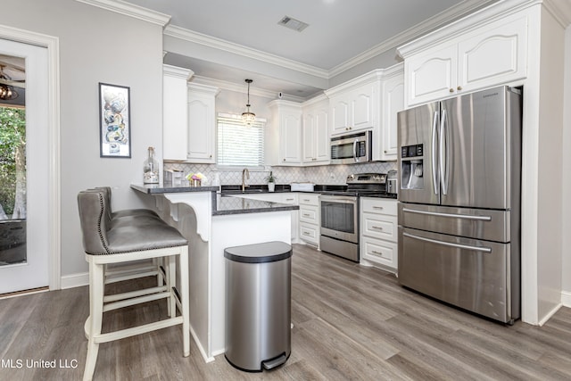 kitchen featuring stainless steel appliances, decorative light fixtures, light wood-type flooring, and white cabinets