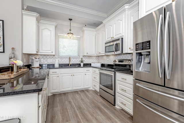 kitchen with appliances with stainless steel finishes, white cabinetry, light hardwood / wood-style flooring, pendant lighting, and sink