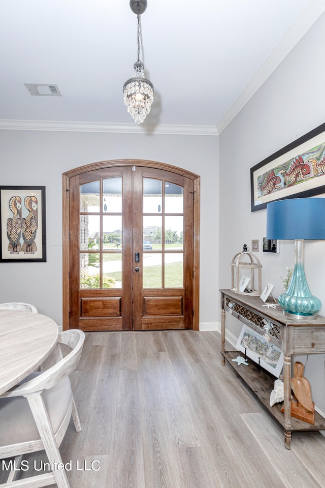 entrance foyer featuring french doors, ornamental molding, a notable chandelier, and light wood-type flooring