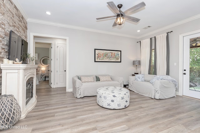 living room with a stone fireplace, crown molding, light wood-type flooring, and ceiling fan