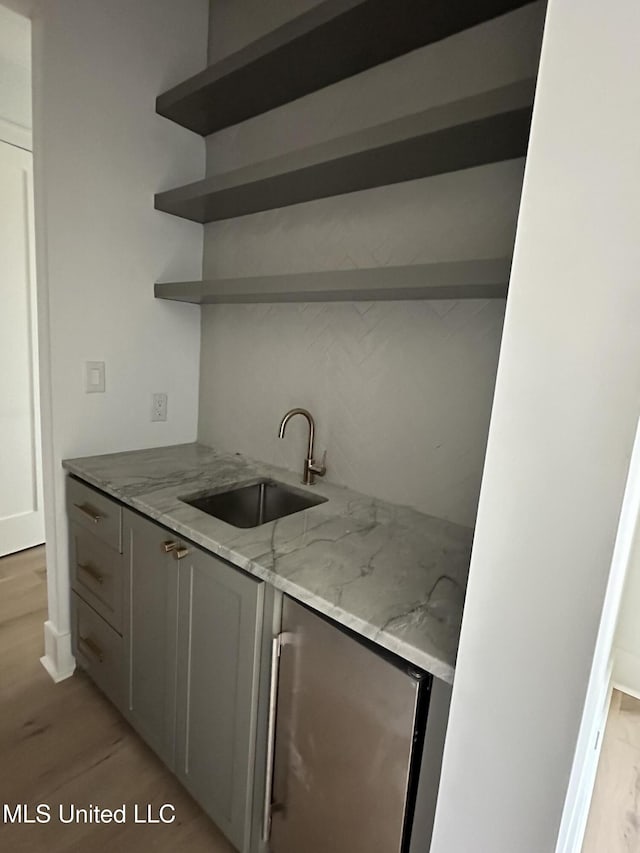 kitchen with light stone countertops, sink, gray cabinetry, and light hardwood / wood-style flooring