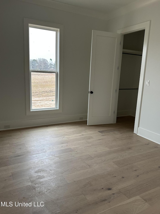 unfurnished bedroom with multiple windows, ornamental molding, a closet, and light wood-type flooring