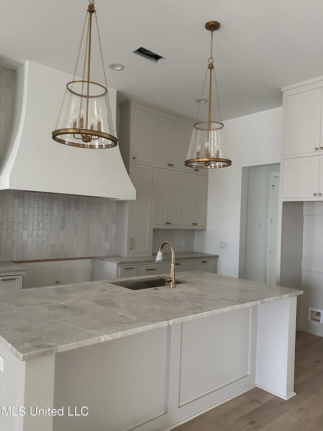 kitchen with pendant lighting, a kitchen island with sink, sink, and light stone countertops