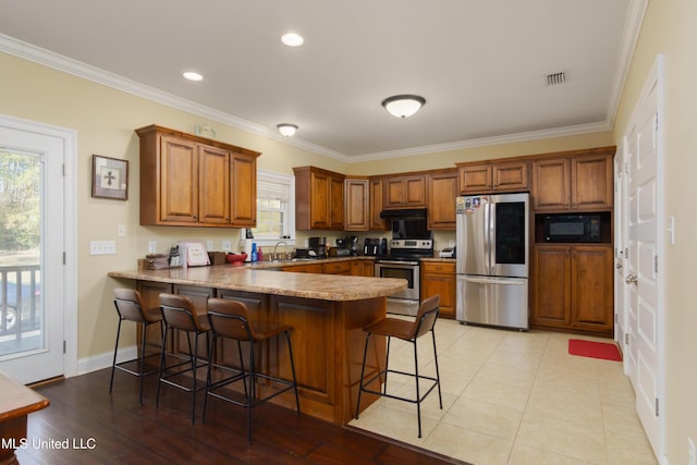 kitchen with sink, kitchen peninsula, crown molding, a breakfast bar, and appliances with stainless steel finishes