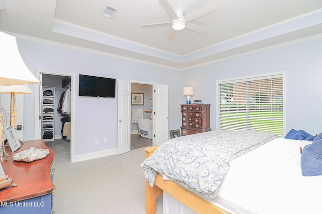 bedroom featuring light carpet, a walk in closet, a tray ceiling, ornamental molding, and a closet