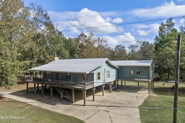back of house with concrete driveway, metal roof, a chimney, and a carport
