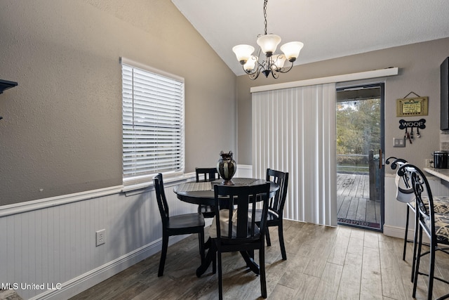 dining area with a textured wall, a chandelier, wood finished floors, and lofted ceiling