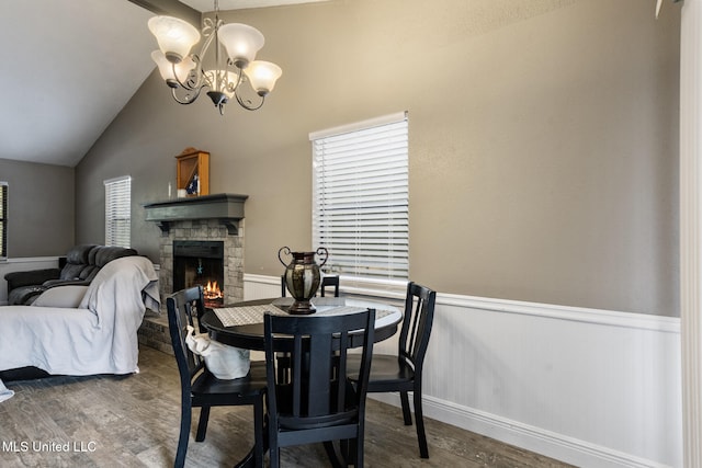 dining room with an inviting chandelier, wood finished floors, a fireplace, a wainscoted wall, and vaulted ceiling