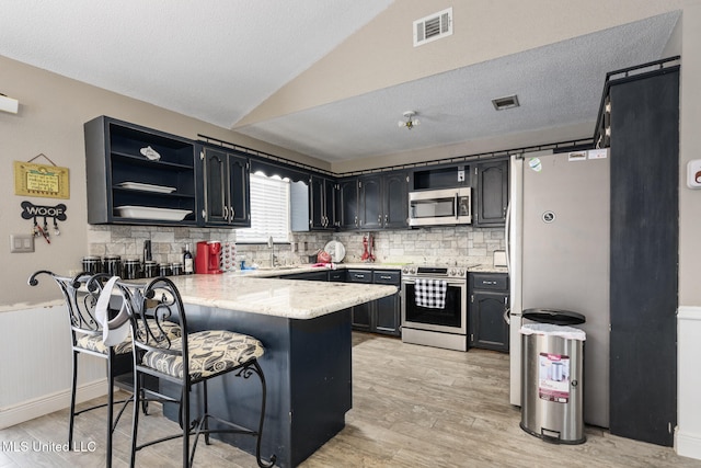 kitchen featuring decorative backsplash, visible vents, appliances with stainless steel finishes, a peninsula, and light wood-style floors
