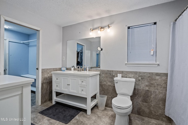 bathroom featuring tile patterned flooring, vanity, wainscoting, tile walls, and a textured ceiling