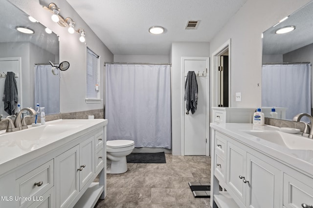 full bath with visible vents, a sink, a textured ceiling, and two vanities