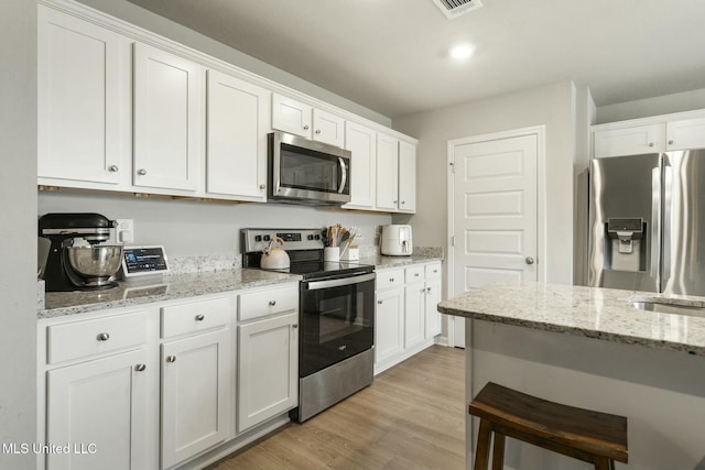 kitchen featuring a breakfast bar, appliances with stainless steel finishes, light hardwood / wood-style floors, light stone counters, and white cabinetry