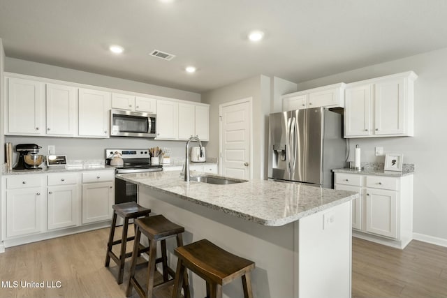 kitchen featuring white cabinetry, sink, a center island with sink, appliances with stainless steel finishes, and light wood-type flooring